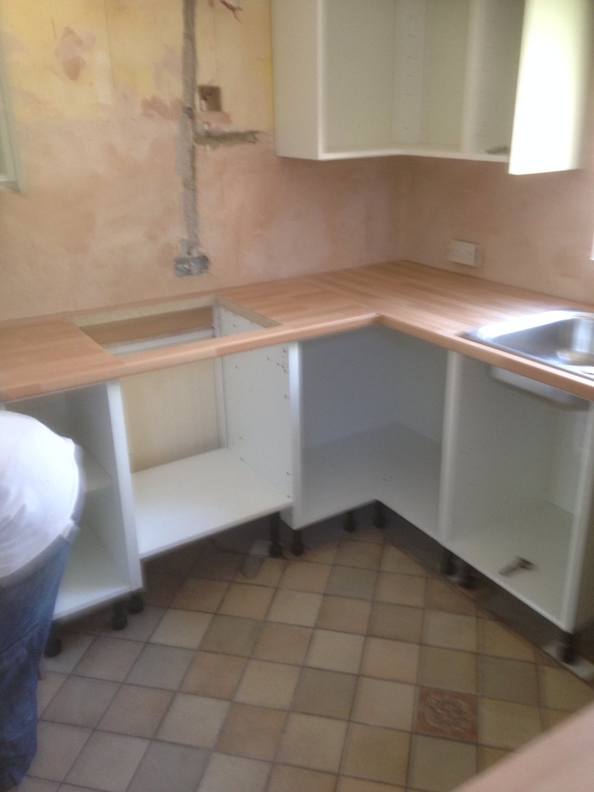 Kitchen units and worktop being installed against a freshly plastered wall
